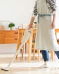 Person wearing an apron cleaning a kitchen and dining room with a stick vacuum cleaner