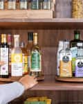 An organized wooden pantry shelf fitted with three wooden turntables holding an assortment of spices, condiments, and other pantry essentials.