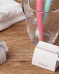 A toothpaste dispenser tool in use on a wooden bathroom countertop