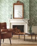 Living room with green floral wallpaper, brown leather chair, wood coffee table, and a mirror above a fireplace with stacked logs.