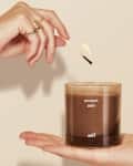 Hand lighting a "sweet ash" candle in a glass jar held by another hand.