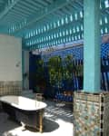 Outdoor patio with a vintage black bathtub, wooden chair, blue pergola, and vibrant tile accents.