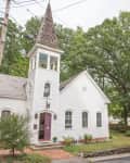 White church with a tall steeple, arched windows, and a red door, surrounded by trees and a brick pathway.