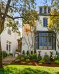 Three-story white house with large bay window, surrounded by trees and landscaped garden.