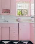 Retro pink kitchen with cabinets, a white sink, pink toaster, plants, and checkered black and white floor tiles.