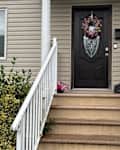 Front entrance with a dark door, decorative wreath, white railings, and potted flowers beside the steps.