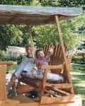 Three children joyfully waving from a wooden swing set.