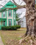 Victorian-style house with green trim, large porch, and bare tree in front yard.