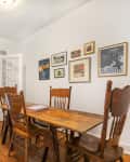 Dining room with wooden table and chairs, gallery wall, and open French doors leading to a kitchen with checkered floor.