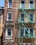 Brick apartment building with green fire escape and potted plants on balconies.