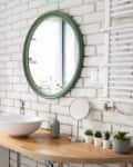 Bright bathroom with a wooden countertop, white bowl sink, green mirror, and decorative plants on shelves.