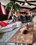 Tropical-themed living room with palm trees, marble table, armadillo decor, and a bar with black stools.