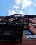 Red brick building with black metal fire escape stairs against a blue sky.