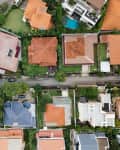 Aerial view of suburban neighborhood with houses featuring red and blue roofs, green lawns, and a swimming pool.