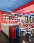 Colorful kitchen and living area with red and blue accents, cherry wallpaper, bookshelves, and city skyline view.