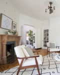 Living room with a fireplace, white armchairs, gray sofa, round table, and potted plants.