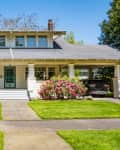 Charming craftsman-style house with a large porch, colorful shrubs, and a car parked in the driveway.