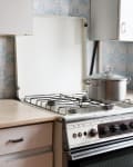 Vintage kitchen with a gas stove, stainless steel pot, and floral blue tile backsplash.