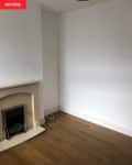 Empty room with a beige fireplace, white walls, and wooden floor.