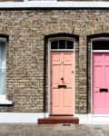 Two adjacent brick house entrances with a peach door on the left and a pink door on the right, each with arched windows above.