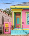 Colorful house with pink walls, turquoise shutters, yellow trim, and a pink door featuring a warning sign.