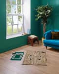 Bright teal living room featuring a tufted blue sofa, decorative rugs, a potted plant, and a window with greenery outside.