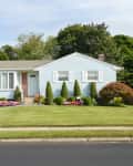 Single-story house with light blue siding, manicured lawn, shrubs, and pink flowers in front yard.