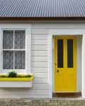 Gray house exterior with a bright yellow door and matching window boxes filled with plants.