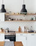 Modern kitchen with white cabinets, wooden countertops, open shelves, and black pendant lights.