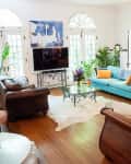 Living room with blue sofa, brown leather chairs, glass coffee table, large mirror, and vibrant plants.