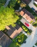 Aerial view of suburban neighborhood with tree-lined streets, parked cars, and houses with brown roofs.