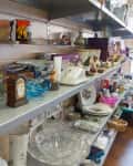 Thrift store shelves with green mugs, vintage clock, glassware, and assorted decorative items.