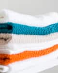 Stacked towels in various colors, including teal, orange, white, and beige, neatly arranged on a shelf.