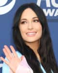 Woman with long dark hair waving, smiling at an awards event.