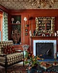 Cozy living room with red walls, a patterned ceiling, a fireplace, and a checkered armchair, adorned with books and decor.