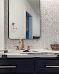 Modern bathroom with dual sinks, black cabinetry, herringbone tile backsplash, and bronze fixtures.