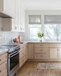 Bright kitchen with light wood cabinets, gray window shades, a floral arrangement, and modern appliances.