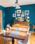 Dining room with blue walls, wooden table, white chairs, wall art, and a piano adorned with plants and candles.
