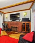 Living room with red sofa, brick fireplace, wall-mounted TV, and wooden ceiling beams.