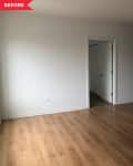 Empty room with light wood flooring, white walls, and a doorway leading to another room.