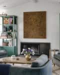 Living room with blue armchairs, green bookshelves, a central fireplace, and a wooden coffee table with a vase of flowers.