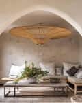 Arched ceiling room with a large rattan light fixture, wooden bench seating, neutral cushions, and a table with greenery.