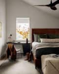 Cozy bedroom with a leather bed, green pillows, desk, chair, boots, and a window with autumn leaves.