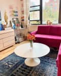 Hot pink sofa, blue rug, and a 1960's tulip table with a pink 80s dresser as a media cabinet in Erica Finamore's NYC apartment