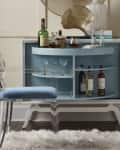 Bar cabinet with blue interior, assorted liquor bottles, glassware, and a clear acrylic chair on a fluffy rug.