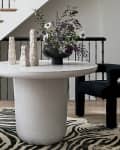 Round white table with black chairs, zebra rug, and floral centerpiece near staircase.
