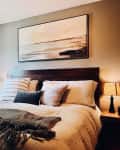 Cozy bedroom with a dark wood headboard, neutral bedding, abstract wall art, and bedside lamps.