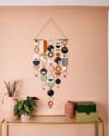 Wall with colorful hanging decor above a console table with plants and vases, adjacent to a dining area.