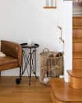 Brown leather chair with a sheepskin throw, black side table, and wicker basket by wooden stairs.