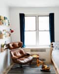 White walled children's bedroom with a striped rug, twin bed, and leather lounger